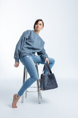 Beautiful woman of model appearance. Girl in grey sweatshirt with black bag on light background....