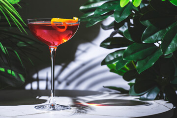 Refreshing red cocktail made with gin, vermouth, and herbal liqueur garnished with an orange twist on a stylish table