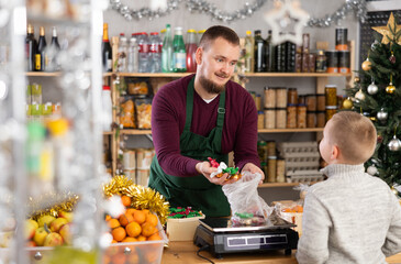 Seller weighs chocolates for a child in a Christmas shop. Boy buys chocolates for the New Year