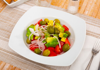 Avocado, tomato, olive, onion, salad served on white plate with serving pieces.