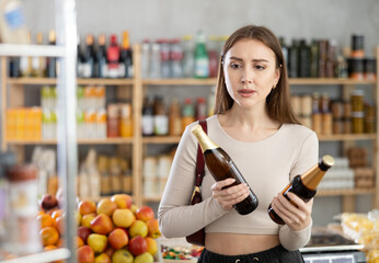 Young woman buyer chooses bottle of beer in grocery store