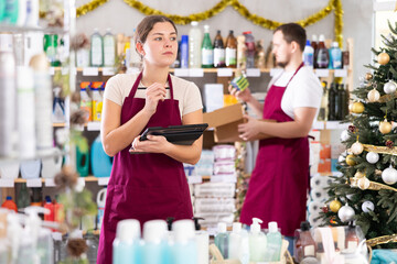 Focused young female household goods store worker using tablet to manage inventory of cleaning...