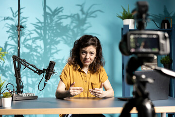 Content creator shooting apology video for disappointed subscribers, doing frantic gesturing trying to excuse herself. Influencer making energetic hand movements, filming with camera