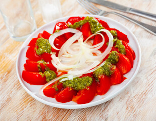 Sliced fresh tomatoes served with basil pesto sauce and onion. Italian style appetizer
