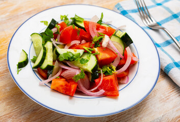Colorful salad with fresh ripe tomatoes, green cucumbers, sliced red onion and herbs. Vegetarian appetizer