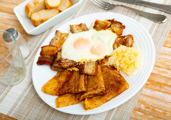Traditional german pancakes with pork bacon, sauerkraut and eggs on a white ceramic plate in a restaurant