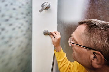 Person in shower enclosure checks lower hose fitting and secures connection to fix water leakage in...