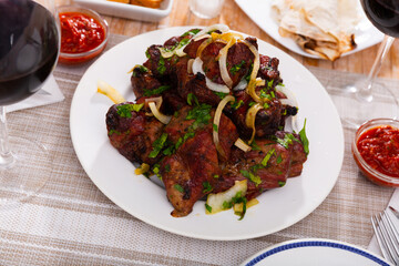 Pork shashlik with onion and greenery served on circular white plate with glasses of wine.