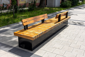 Modern wooden street bench with metal base and split backrest on tiled pavement in urban park...