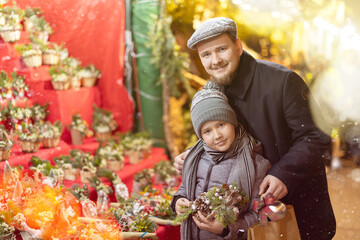 Near counter, dad and son are looking at crafts and bouquets of pine branches and eucalyptus...