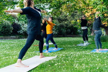 Female yoga class in park. Group of diverse women doing stretching pose exercising together with instructor on green grass lawn. Sport activity for health, wellbeing, mental health. Selective focus