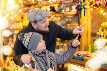 Man with son among crowd of shoppers at holiday fair. Buyers by outdoor souvenir shop window...