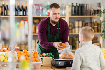 Caring middle-aged male seller weighing and selling tangerines for little boy in local market