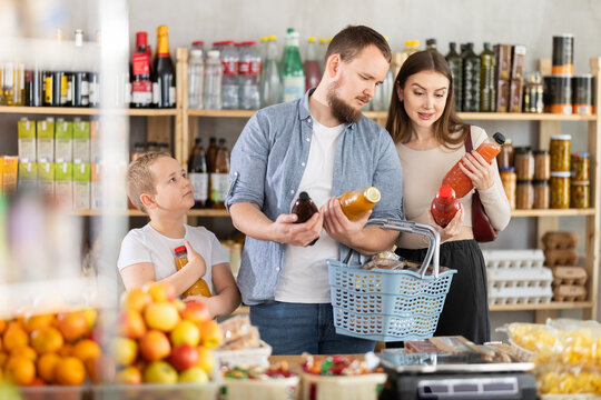 Interested preteen boy standing together with father and mother in grocery store, holding colorful juice bottles while deciding on purchase
