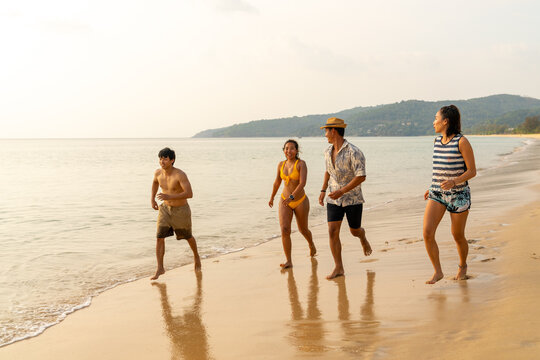 Happy Asian man and woman travel nature the sea on summer beach holiday vacation. Group of People friends enjoy and fun outdoor lifestyle walking and playing together on tropical beach at sunset.