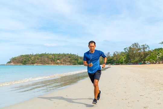 Asian man in sportswear and smartwatch jogging exercise on tropical beach. Healthy guy enjoy outdoor active lifestyle sport training fitness workout running at seaside. Wellness healthcare motivation.