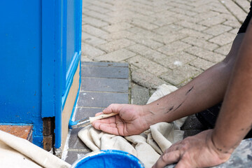 Hand of Decorator with paintbrush painting wood door frame with blue paint