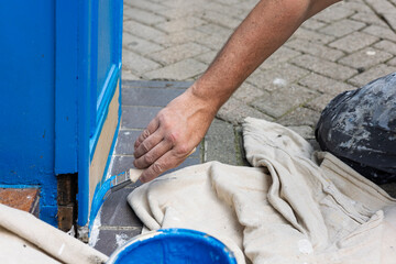 Hand of Decorator with paintbrush painting wood door frame with blue paint