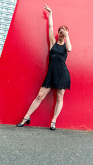 Red wall dancer posing with one arm up and covering her face