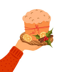 Hand holding a wooden board with traditional Italian panettone bread, decorated with dried citrus slices, holly leaves, red berries, and cinnamon sticks. For Christmas greeting cards, bakery ads