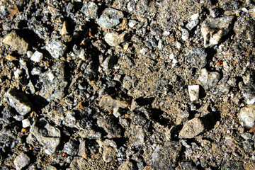 close-up of a gravel and crushed stone aggregate road surface with weathering and wear from traffic. abstract texture background with copy space