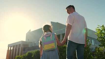 father holds hand little first-grader, child kid girl daughter goes to school backpack holding father hand, happy family, school building glare sun, first-grader school bag goes education building - Powered by Adobe