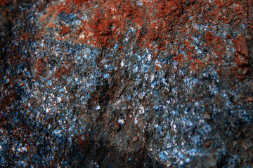 a close-up view of a textured rock surface, with reddish-brown rusty material and shimmering...