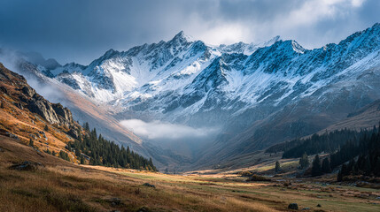 Obraz premium Majestic snowy mountains rise above alpine valley. Coniferous trees dot scenic landscape. Ideal for travel, adventure, nature marketing, web design.
