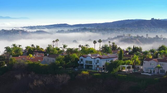 Experience stunning aerial views of Calabasas, California in the early morning, highlighting misty hills and luxury homes under a vibrant blue sky, creating a tranquil and picturesque landscape