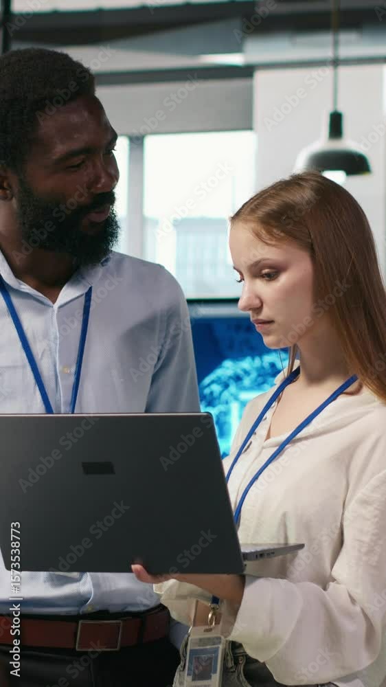 Poster vertical video junior dev and colleague in office reviewing ai system metrics, monitoring performanc