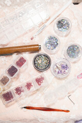 Nail art supplies for home beauty treatment and fashion include rhinestones, glitter, and brushes arranged on lace fabric creating elegant salon atmosphere