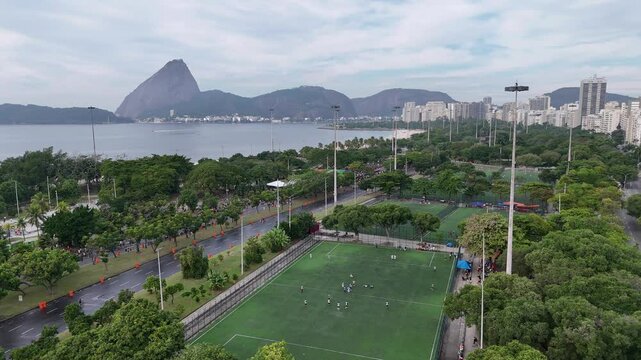 Drone view of Flamengo Park in Rio with football fields, urban skyline, and Sugarloaf Mountain by Guanabara Bay.