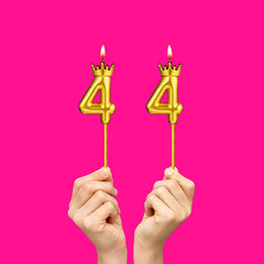 Birthday on a fuchsia background with the number 44 - Hands holding number-shaped candles