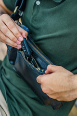 A man's hand inserts a vehicle remote key into a small leather bag, perfect for a leather products catalog design.