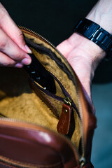 A man's hand inserts a vehicle remote key into a small leather bag, perfect for a leather products catalog design.