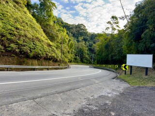 Estrada de rodovia com uma curva e placa de sinalização em branca para personalizar.