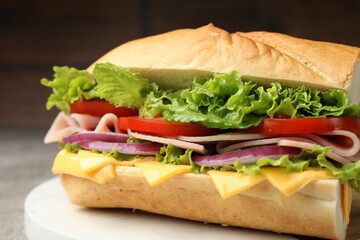 Tasty baguette sandwich with ham, cheese and vegetables on grey table against blurred brown...