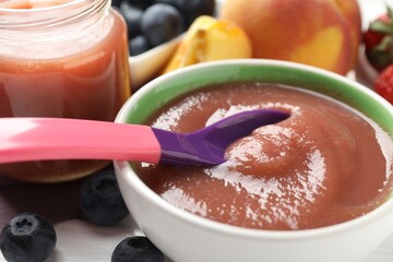 Baby food. Eating tasty puree with spoon at white wooden table, closeup