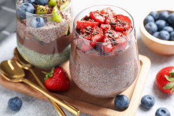 Delicious chocolate puddings with chia seeds and berries in glasses on grey table, closeup