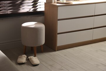 Stylish pouf and slippers near chest of drawers at home