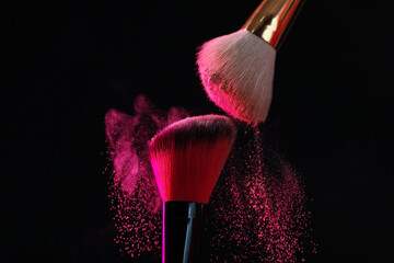 Makeup brushes with pink eye shadow on black background, closeup
