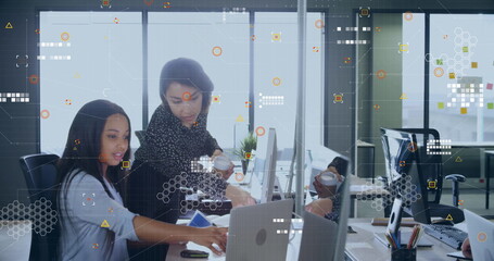 Collaborating two women pointing at laptop on office desk, with coffee cup, copy space