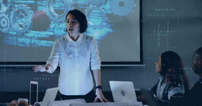 Presenting woman in business attire gesturing at projection screen in meeting room with laptops - Powered by Adobe