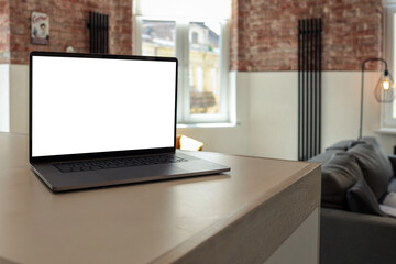 Modern loft-style living room with a laptop on the kitchen counter, exposed brick walls, cozy armchair, and natural light coming through large windows
