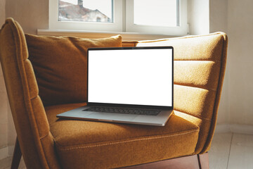 Laptop with blank screen on a cozy mustard armchair by the window, illuminated by warm natural...