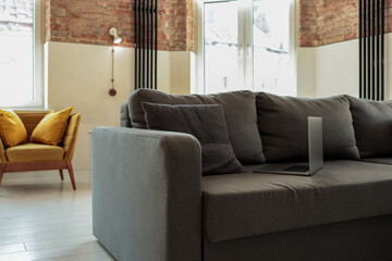 Modern loft living room with a gray sofa, laptop, decorative pillows, brick walls, and large...