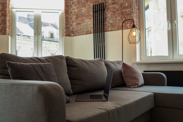 Modern loft living room with a gray sofa, laptop, decorative pillows, brick walls, and large...