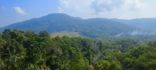 Panoramic view of rolling, tree-covered mountains and dense, vibrant green jungle. The clear sky...