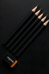Minimalist top view of six black wooden pencils aligned next to a black and orange sharpener on a dark background, perfect for creative, educational, or design-related themes

