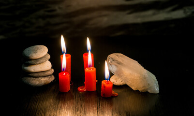 Velas rojas encendidas junto a cristales de cuarzo y piedras en equilibrio sobre fondo oscuro